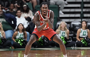 Antoine Davis claps his hands and yells while wearing a red ɫۺϾþ Mercy uniform. Cheerleaders and other people are pictured behind him inside of an arena.