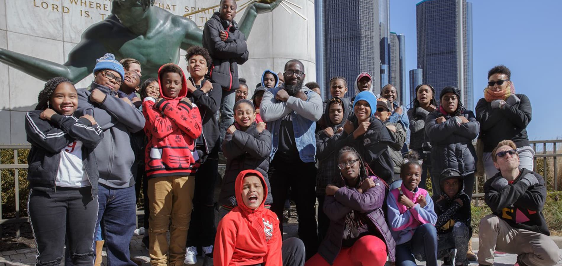 Michael Ford stands outdoors in front of an iconic statue in downtown ɫۺϾþ, surrounded by more than a dozen children in sweatshirts and coats.