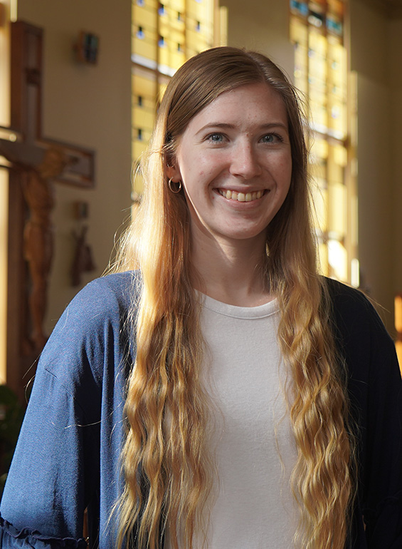 MacKenzie Patterson stands and smiles inside of St. Ignatius Chapel with the sun shining in.